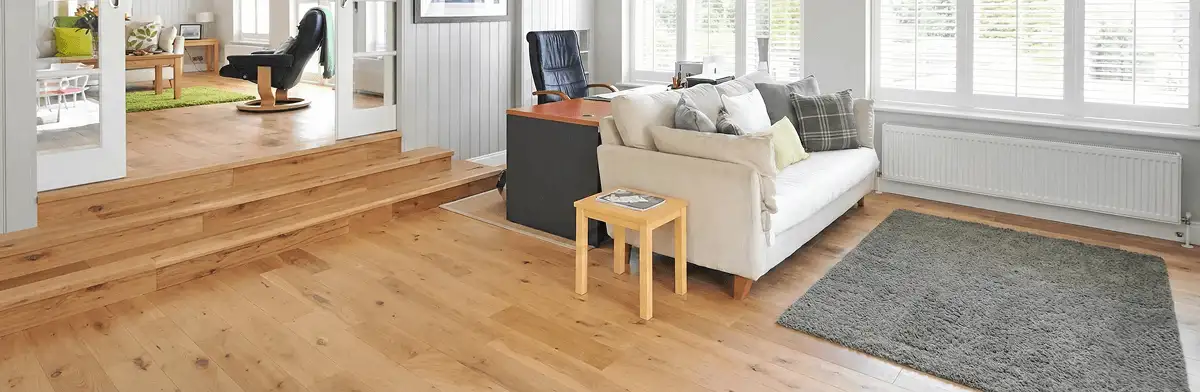 A modern living room with professionally installed laminate flooring, a beige sofa, a small side table, a gray rug, and large windows with white shutters in Oklahoma City, OK